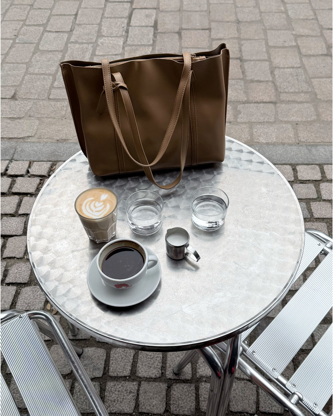 Modelfoto af brun AYLEEN taske, stående på cafebord. Alt er fra BySofieSønderby