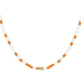 Halskæde af perler, vekslende mellem hvide og orange farver, med en lille guld detalje i midten. Ligger mod en simpel hvid baggrund.