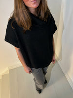 En person iført sort sweater står på en gråmalet trappe. Personen er delvist uden for billedet, med langt brunt hår og grå bukser. Væggen er hvid baggrund.