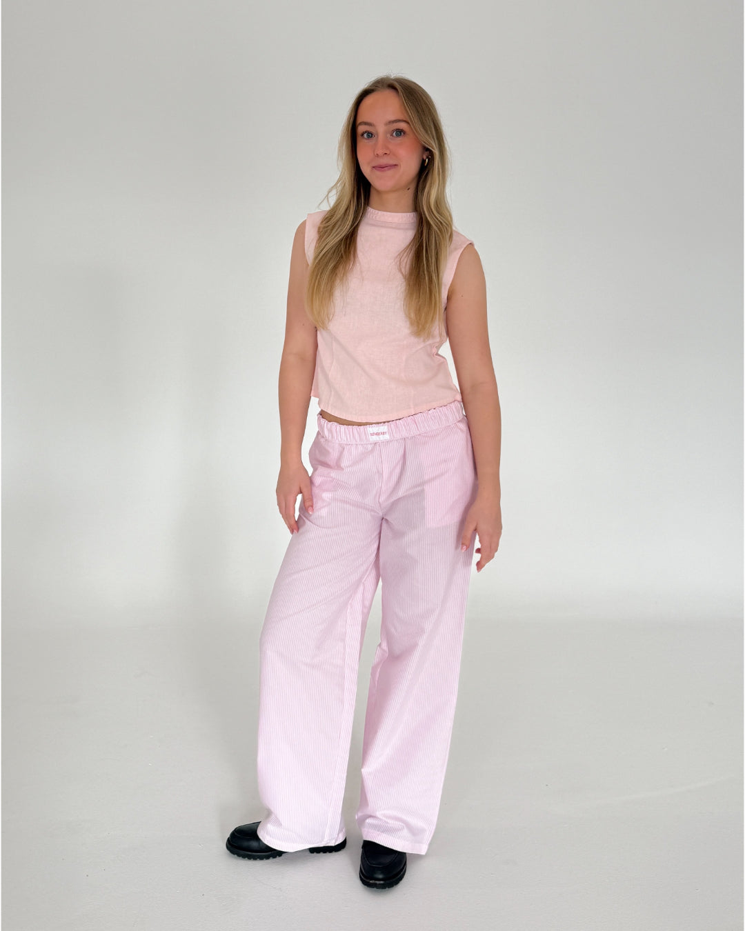 Modelfoto af pige i lyserødstribede CAJSA bukser, samt lyserød ANNIKA top. Alt er fra BySofieSønderby