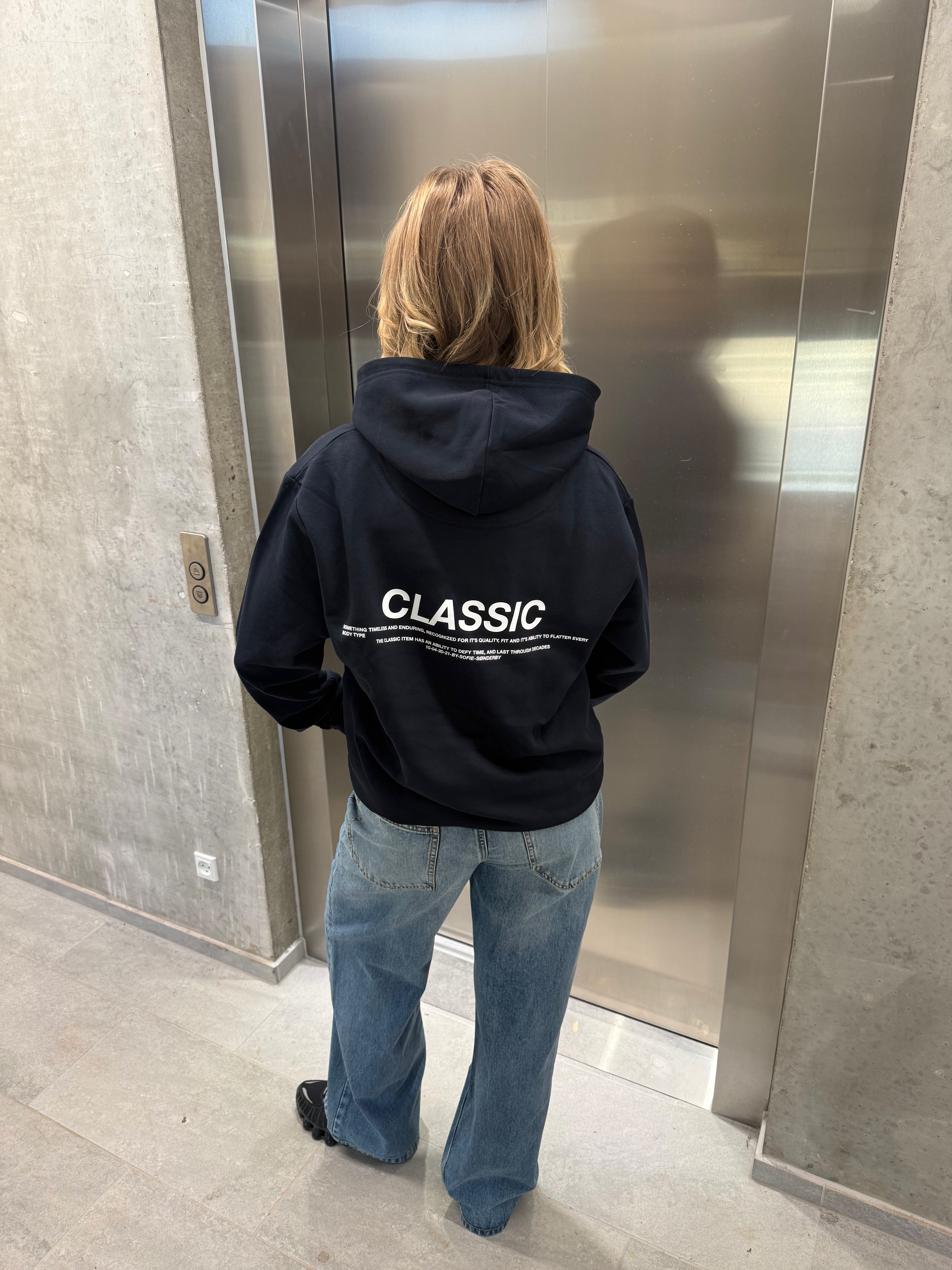 Stemningsbillede af pige der bærer en navy hoodie med hvidt classic tryk og blå NANNA jeans.  Fra BySofieSønderby
