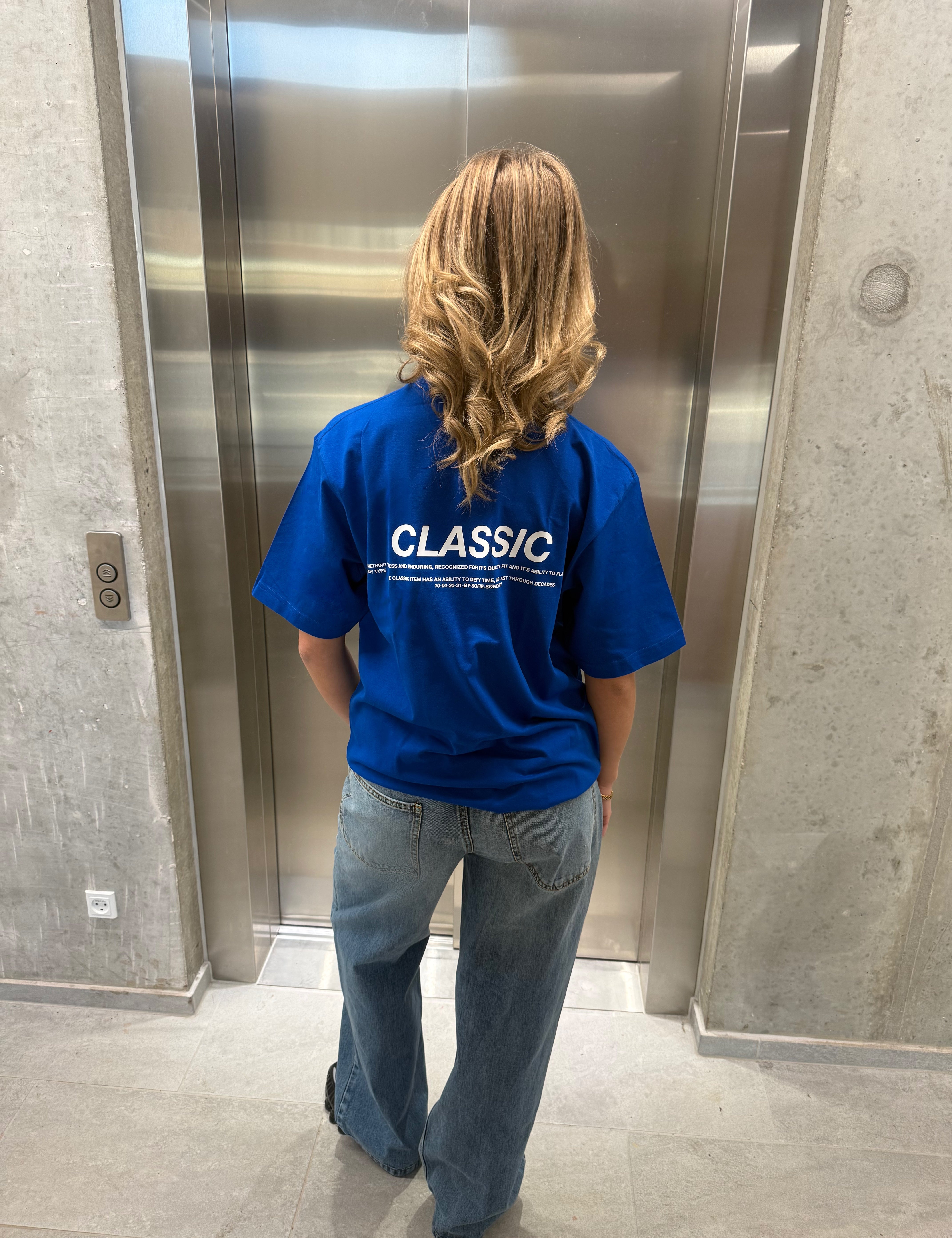 Stemningsbillede af pige der bærer en kongeblå t-shirt med hvidt classic tryk og blå NANNA jeans.  Fra BySofieSønderby