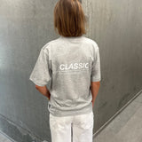 Stemningsbillede af pige der bærer en grå t-shirt med hvidt CLASSIC tryk og hvide NANNA jeans.  Fra BySofieSønderby