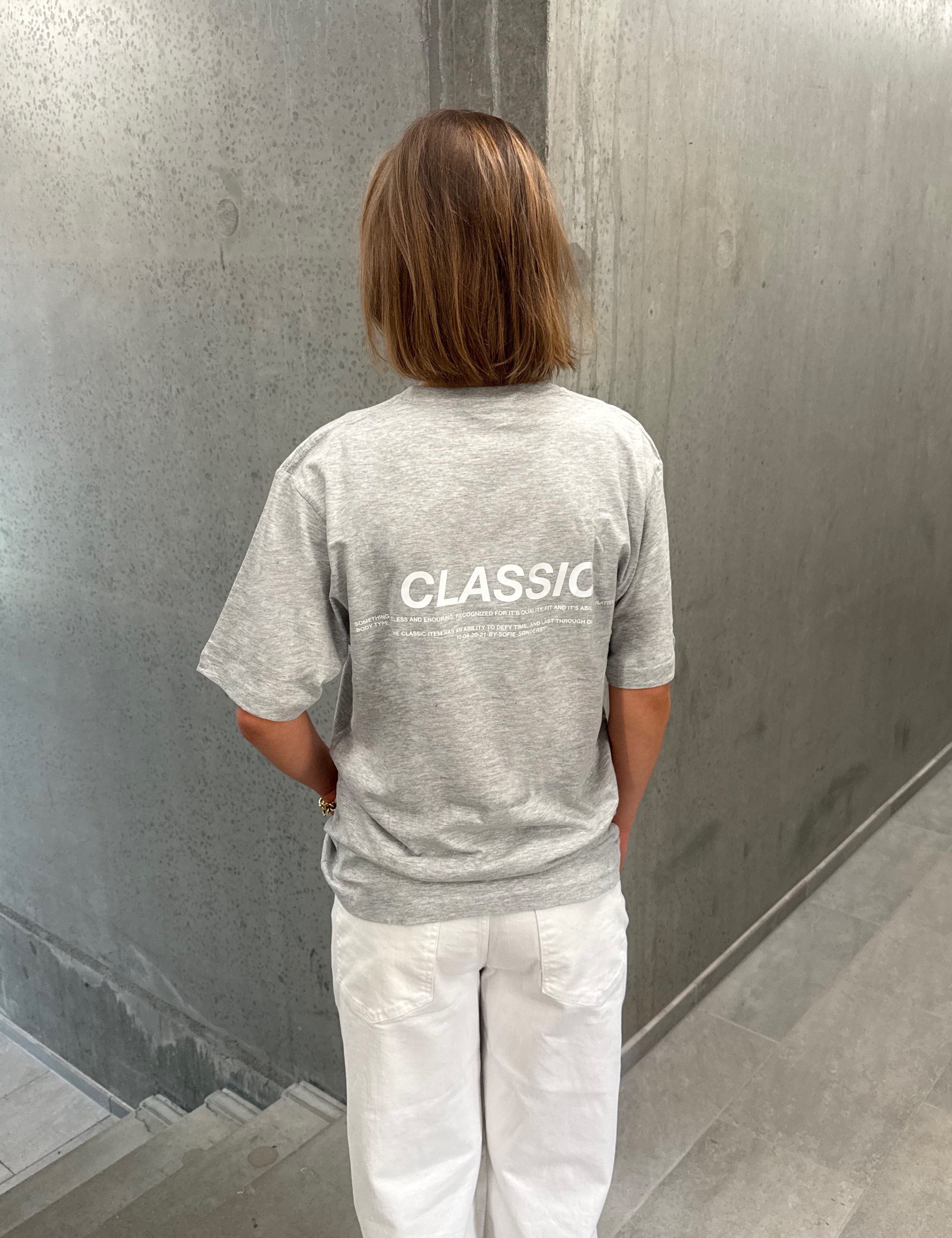 Stemningsbillede af pige der bærer en grå t-shirt med hvidt CLASSIC tryk og hvide NANNA jeans.  Fra BySofieSønderby
