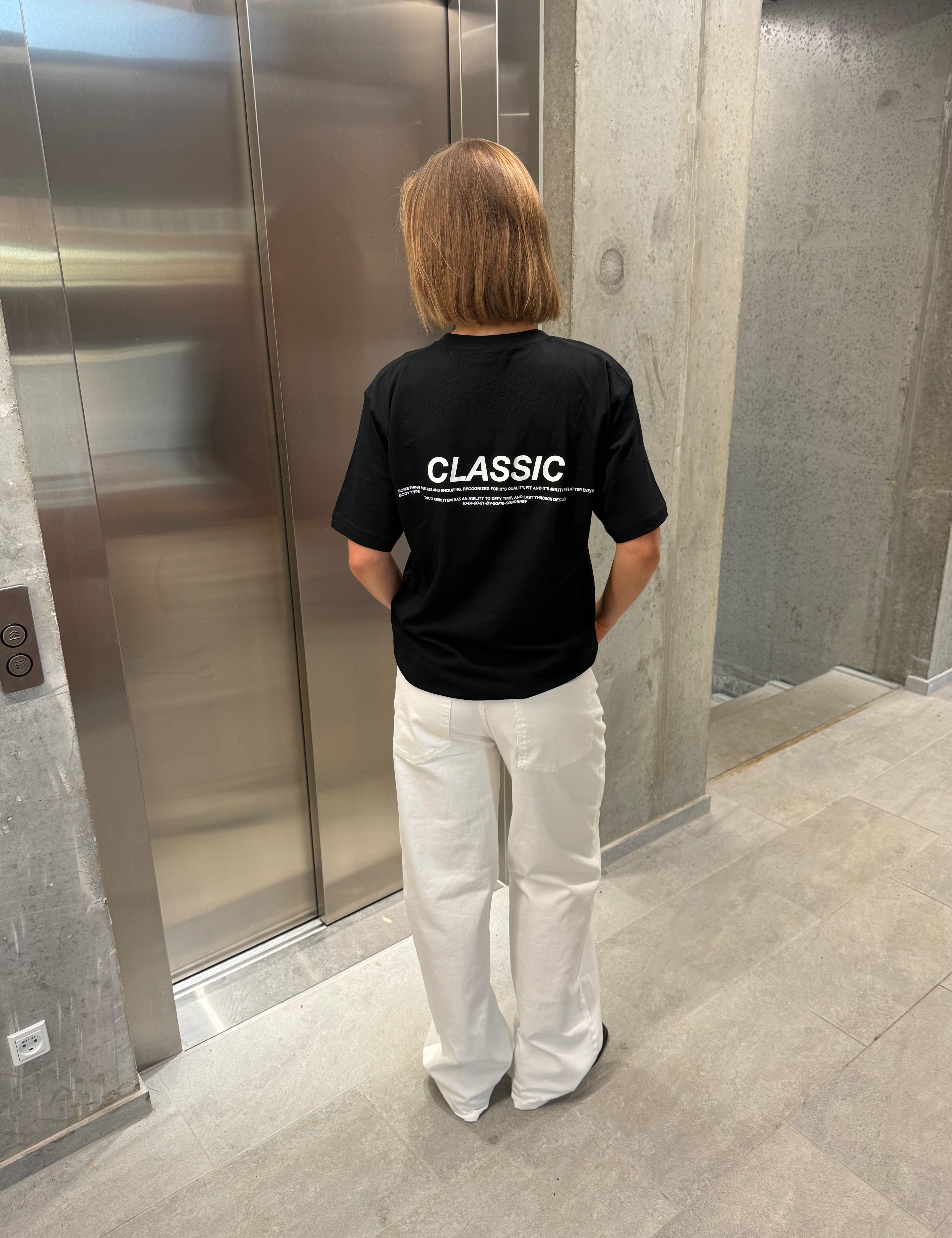 Stemningsbillede af pige der bærer en sort t-shirt med hvidt classic tryk og hvide NANNA jeans.  Fra BySofieSønderby