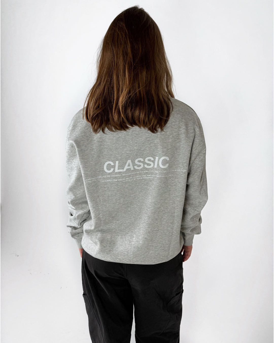Modelfoto af pige i grå CLASSIC sweatshirt med hvid tryk på ryggen. Modellen ses bagfra. Alt er fra BySofieSønderby