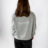 Modelfoto af pige i grå CLASSIC sweatshirt med hvid tryk på ryggen. Modellen ses bagfra. Alt er fra BySofieSønderby