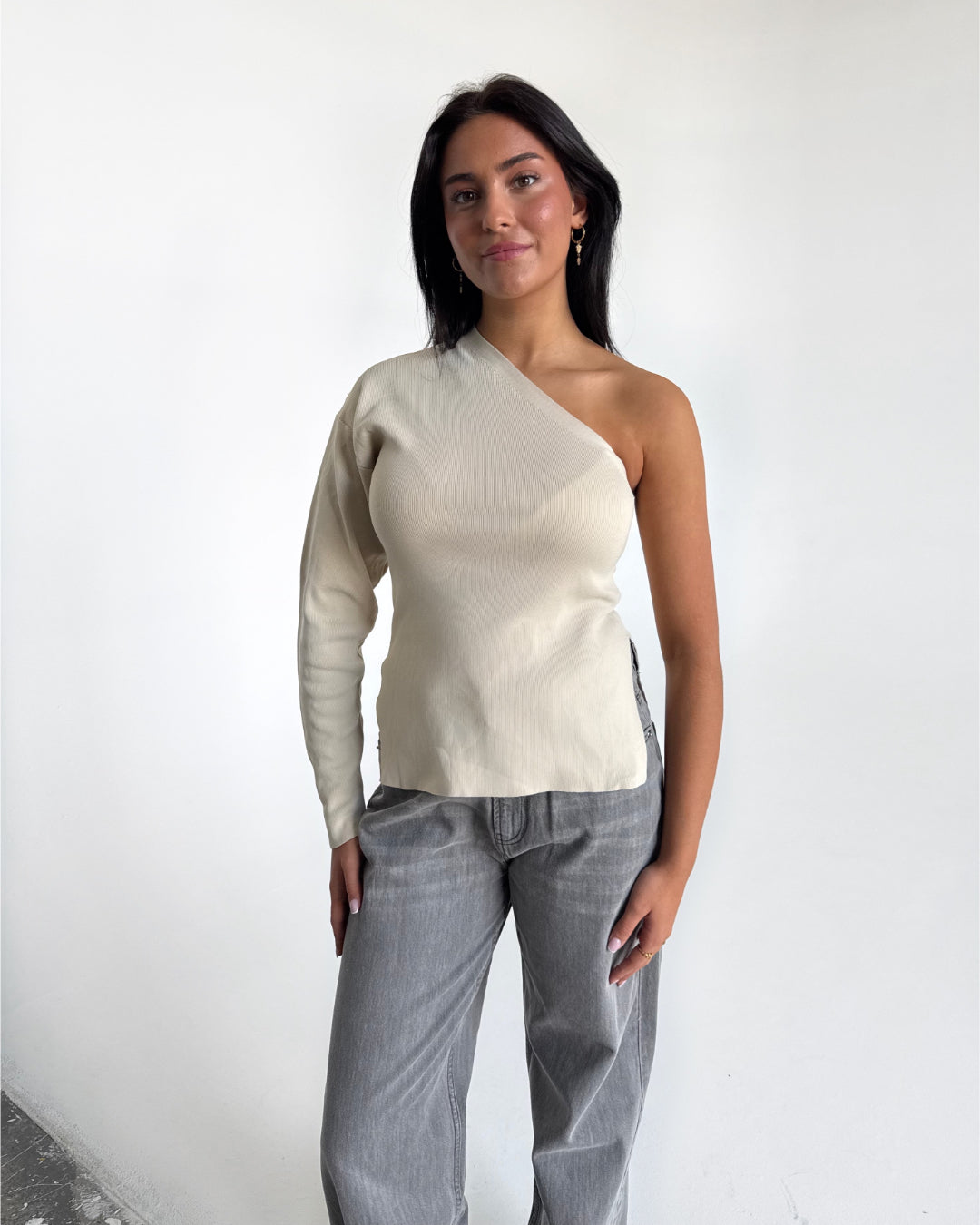 Modelfoto af pige i cremefarvet COLLINS one-shoulder, samt grå NANNA jeans. Alt er fra BySofieSønderby