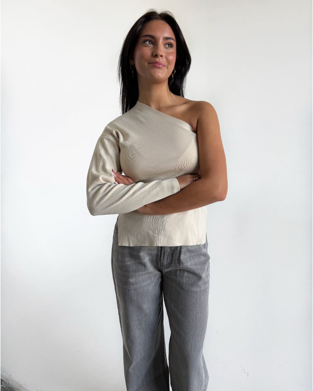 Modelfoto af pige i cremefarvet COLLINS one-shoulder, samt grå NANNA jeans. Alt er fra BySofieSønderby