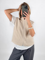 Modelfoto af pige i beige DAWN vest, hvid t-shirt og grå LISA bukser. Alt er fra BySofieSønderby.