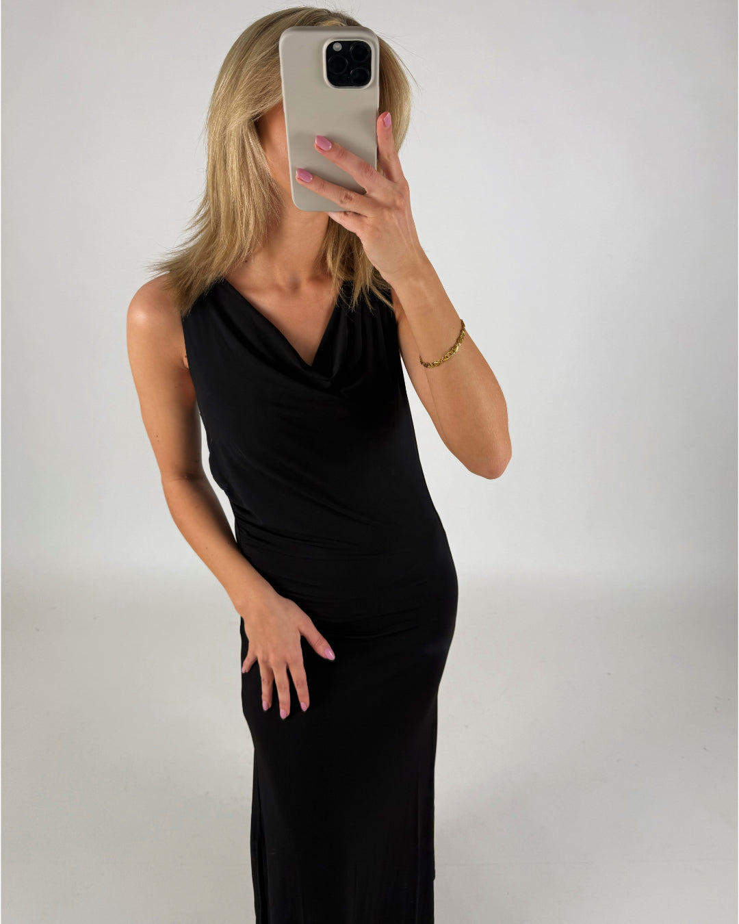 En person i en sort kjole tager et selfie med en smartphone. Personen har blond hår og neglelak, og rummet har en lys baggrund.