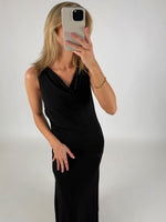 En person i en sort kjole tager et selfie med en smartphone. Personen har blond hår og neglelak, og rummet har en lys baggrund.