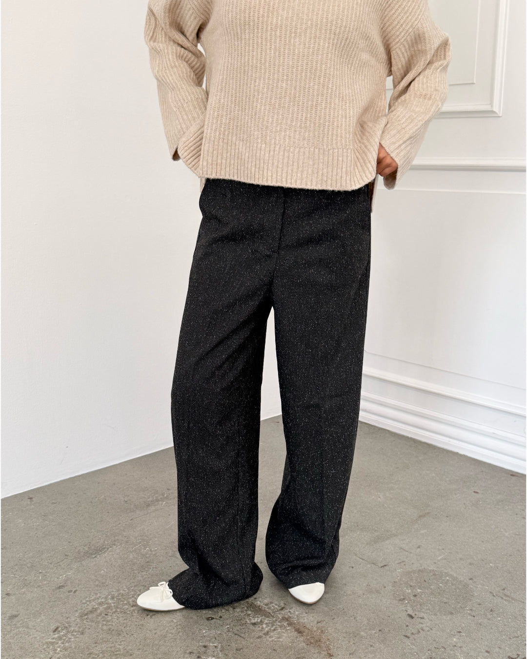 Modelfoto af pige i sort melerede ELLIS bukser, samt beige striktrøje. Alt er fra BySofieSønderby.