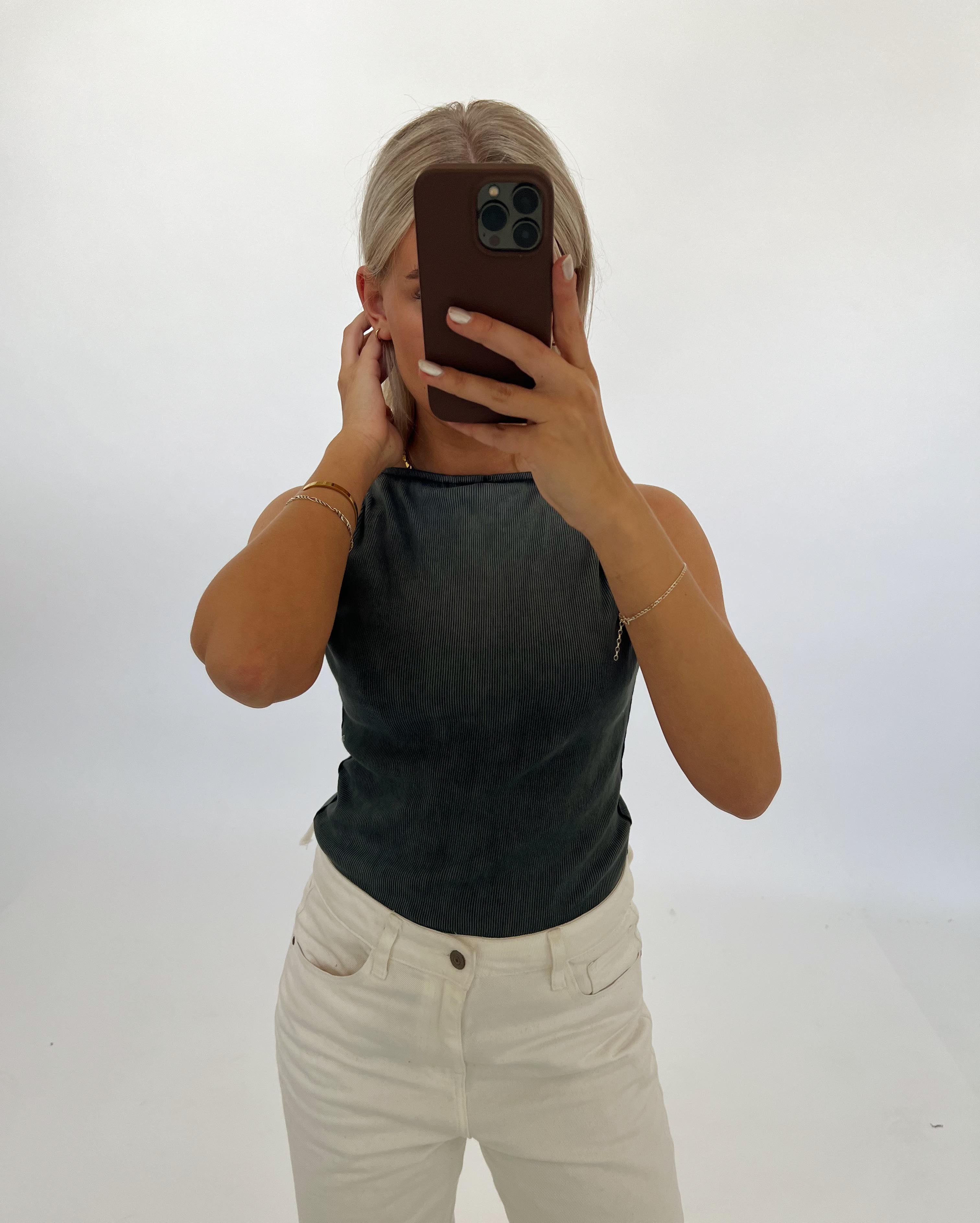 En person tager et spejlbillede med en smartphone. Personen bærer en sort top og hvide bukser. Baggrunden er hvid og minimalistisk.