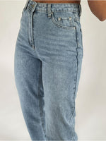 Et par lyseblå jeans bæres, med fokus på hofte- og lommedetaljer. Jeansene har en høj talje, lynlåsgylp og sidder i et neutralt studio-tagningsmiljø med hvid baggrund.