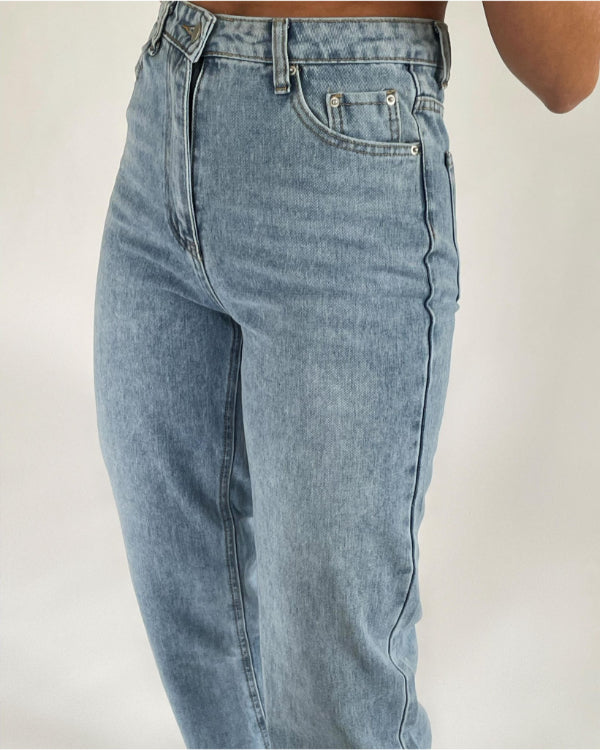 Et par lyseblå jeans bæres, med fokus på hofte- og lommedetaljer. Jeansene har en høj talje, lynlåsgylp og sidder i et neutralt studio-tagningsmiljø med hvid baggrund.
