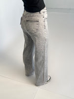 Grå jeans bæres af en person iført sort bluse og grønne sko. Personen står i et lysegråt rum med hvidt gulv.