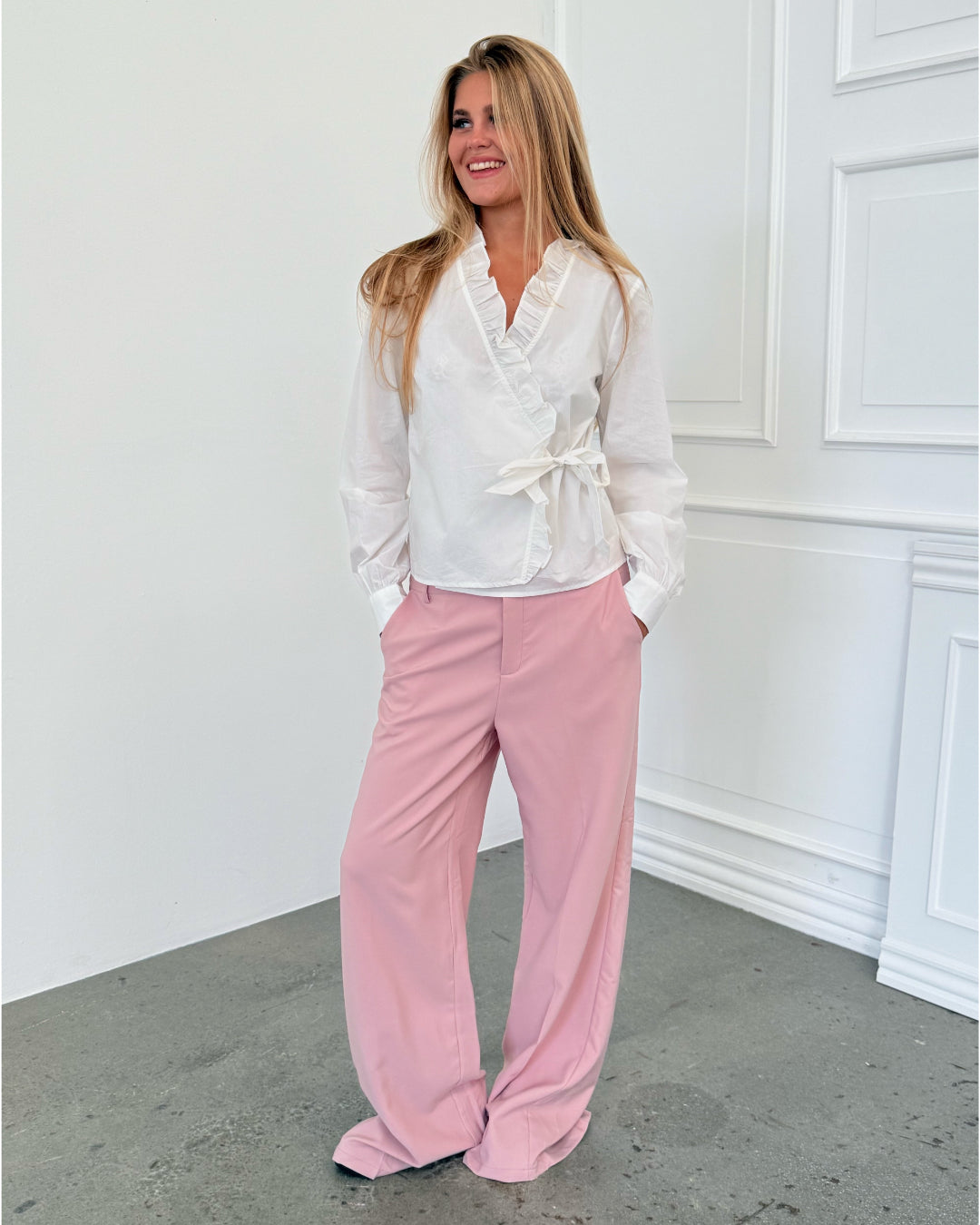 Modelfoto af pige i hvid HOPE skjorte, samt lyserøde SELENA bukser. Alt er fra BySofieSønderby.