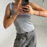 En person i grå top og bukser tager et spejlbillede med en smartphone. Personen bærer gyldne smykker, og omgivelserne er minimalistiske og lyse.