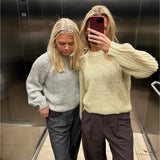 To personer i striktrøjer står i en elevator med et spejl. Den ene tager et selfie med en smartphone. Elevatorens blanke metalvægge og flisegulv ses omkring dem.