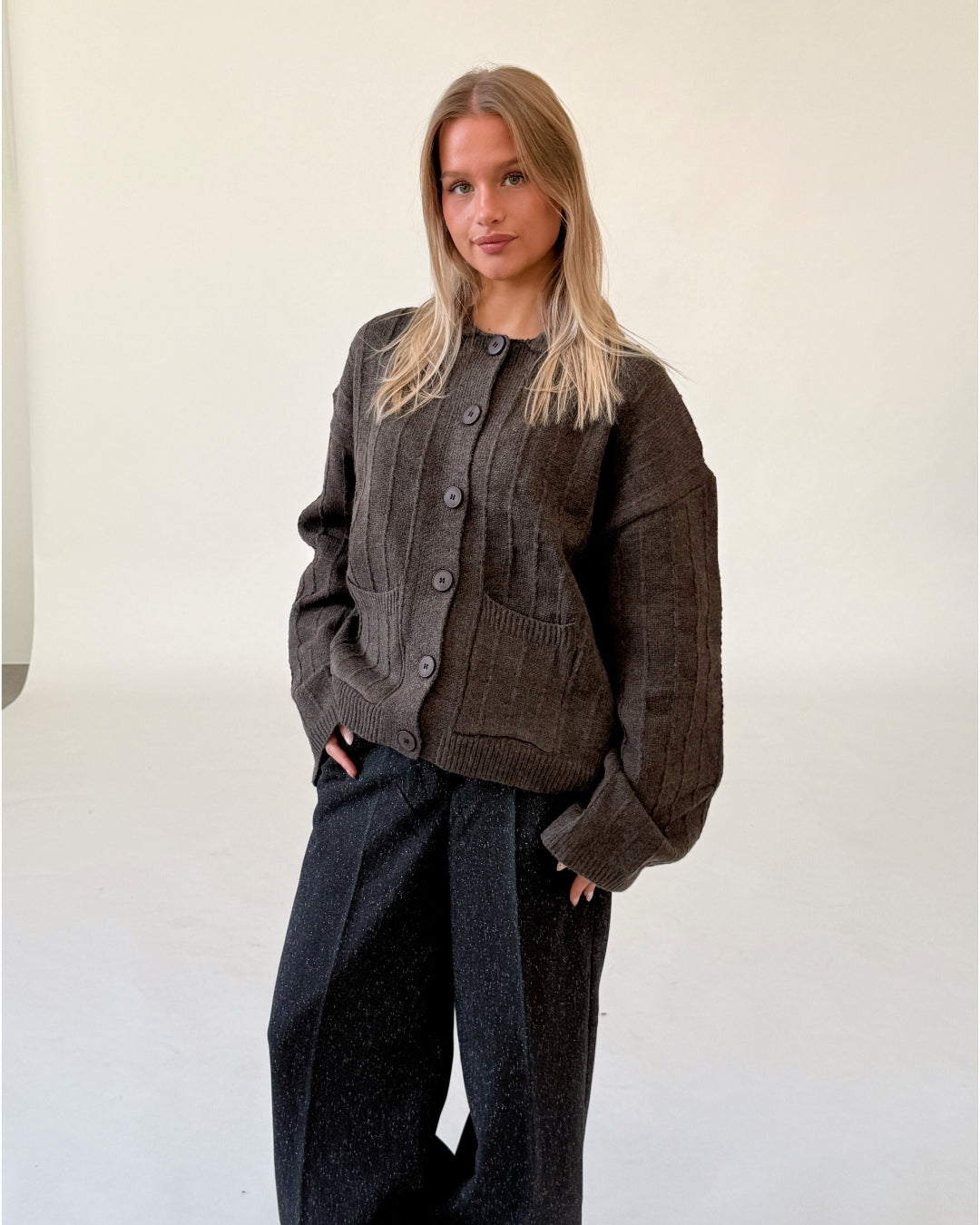 Modelfoto af pige i brun LACEY cardigan, samt sortmelerede ELLIS bukser. Alt er fra BySofieSønderby.