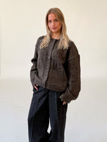 Modelfoto af pige i brun LACEY cardigan, samt sortmelerede ELLIS bukser. Alt er fra BySofieSønderby.
