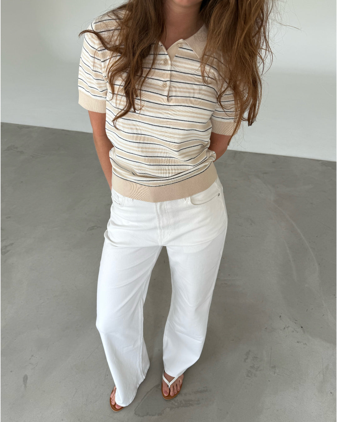 Modelfoto af pige som bærer en LILLIANA beigestribet polo t-shirt og hvide jeans. Alt er fra BySofieSønderby