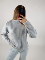 En person iført en lyseblå, stribet sweater tager et billede med en sort telefon. Personen er omgivet af en lys, neutralt farvet baggrund.