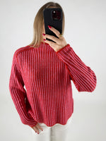 En person iført en rød- og pinkstribet sweater tager et spejlbillede med en sort mobiltelefon. Personen har rød neglelak og bærer en ring. Baggrunden er enkel og lys.