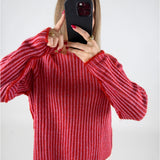 En person holder en sort telefon op foran ansigtet iført en rødstribet sweater, omgivet af en lys baggrund. Personen viser pegefingeren på telefonens skærm.