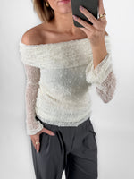 Modelfoto af pige i cremefarvet MAISY off-shoulder blondebluse og grå LISA bukser. Alt er fra BySofieSønderby.