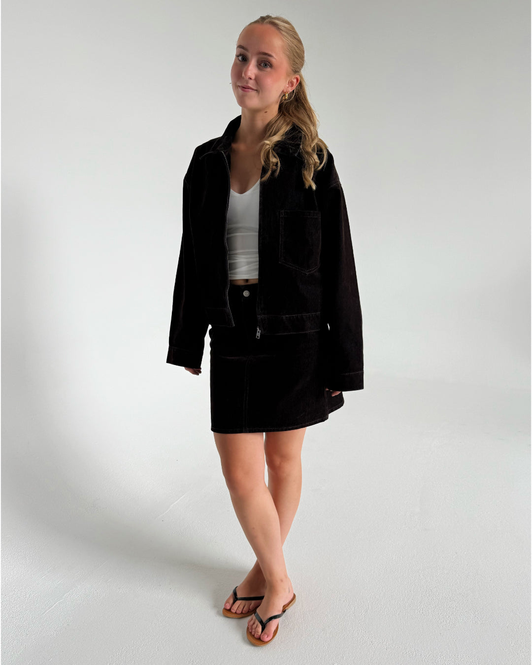 Modelfoto af pige der bærer Mia jakke i brun uden på en hvid top og Mia nederdel i brun. Alt fra BySofieSønderby