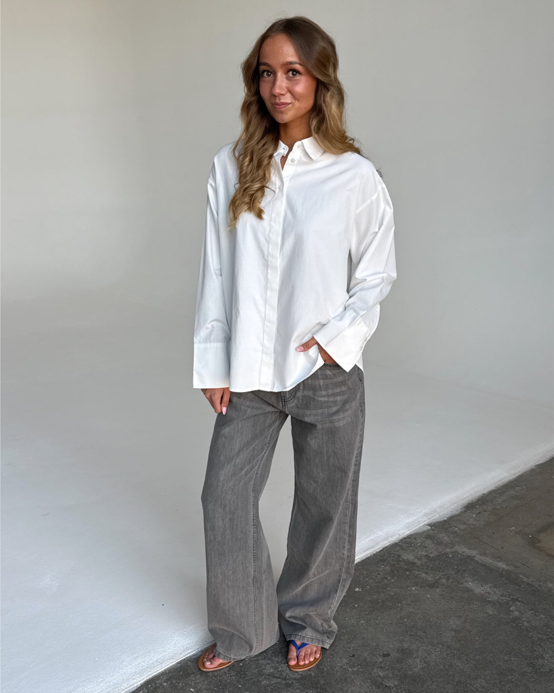Modelfoto af pige i grå NANNA jeans og hvid CARO skjorte. Alt er fra BySofieSønderby.