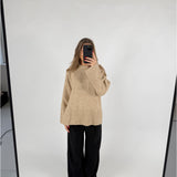 En person står i et lyst rum og tager et spejlbillede iført en beige sweater og sorte bukser. Telefonen dækker ansigtet.
