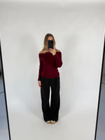 En person tager et spejlbillede af sig selv iført en bordeaux bluse og sorte bukser i et lyst rum. Der er ingen tekst.