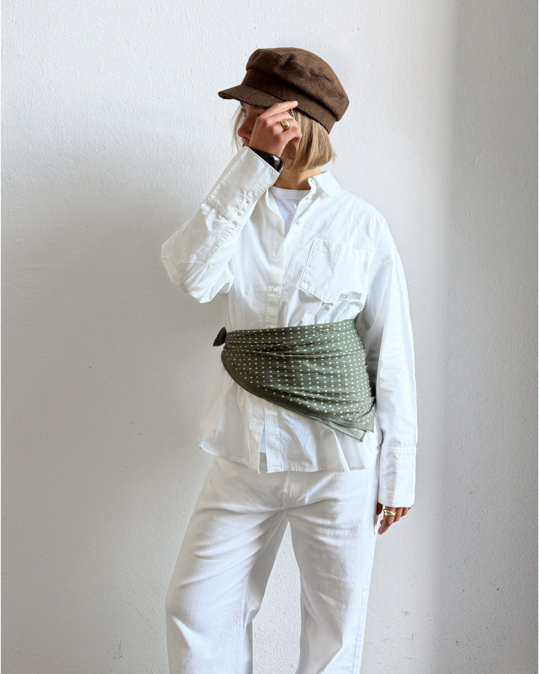 Modelfoto af pige i kaki ROSALINA tørklæde bundet om livet. Desuden bærer hun hvid CARO skjorte og hvide NANNA jeans. Alt er fra BySofieSønderby.