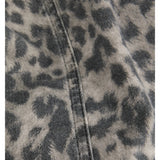 Grå og sort leopardmønstret stof ligger foldet med en synlig søm. Stoffet ser jævnt ud, hvilket tyder på tøj eller tekstil i blødt materiale.