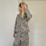 En person iført et zebra-mønstret sæt tøj står med hånden i håret foran en hvid dør i et minimalistisk rum.