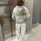 Stemningsbillede af pige der bærer en grå hoodie med army SNDRB tryk og hvide NANNA jeans.  Fra BySofieSønderby
