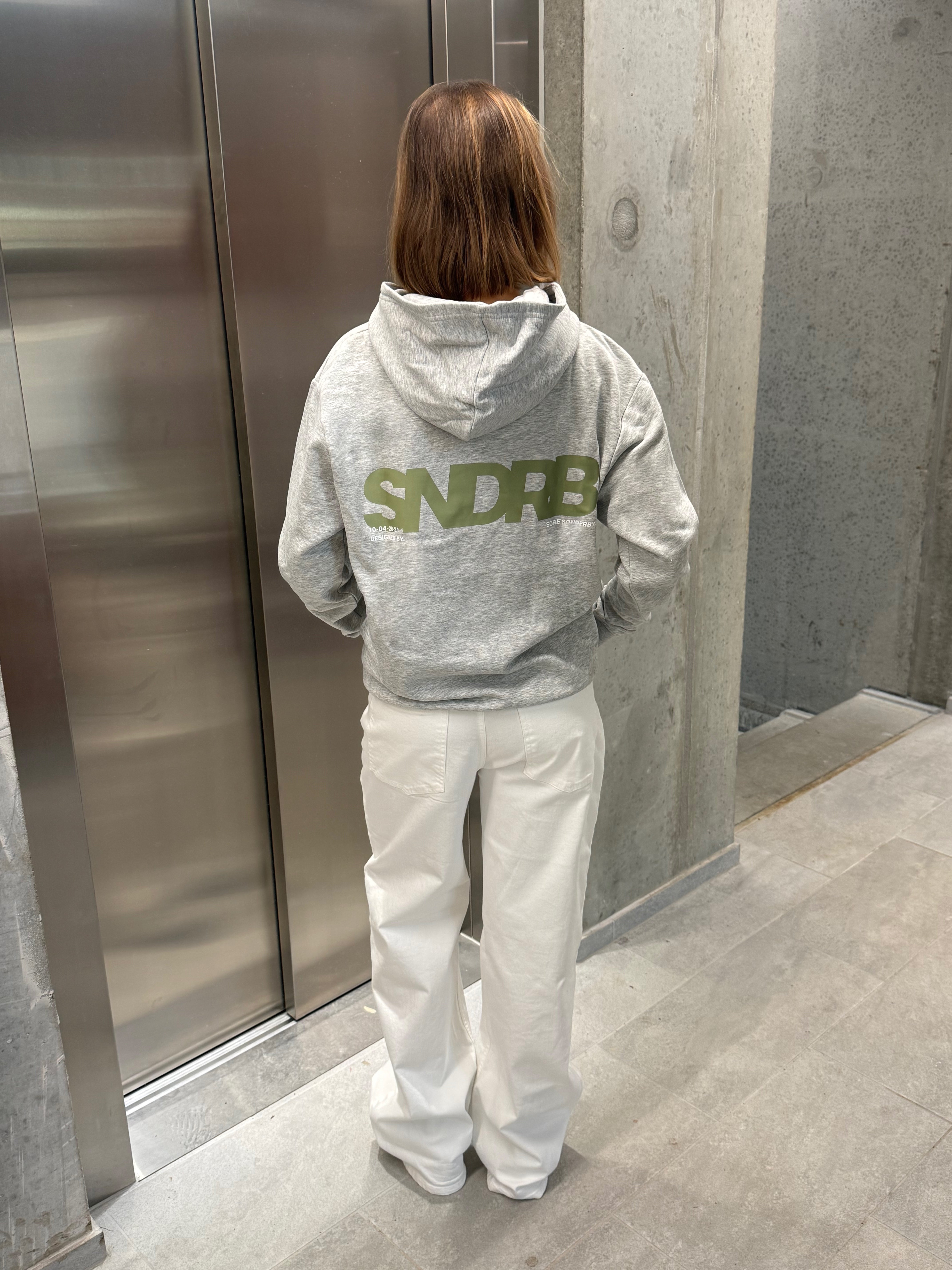 Stemningsbillede af pige der bærer en grå hoodie med army SNDRB tryk og hvide NANNA jeans.  Fra BySofieSønderby