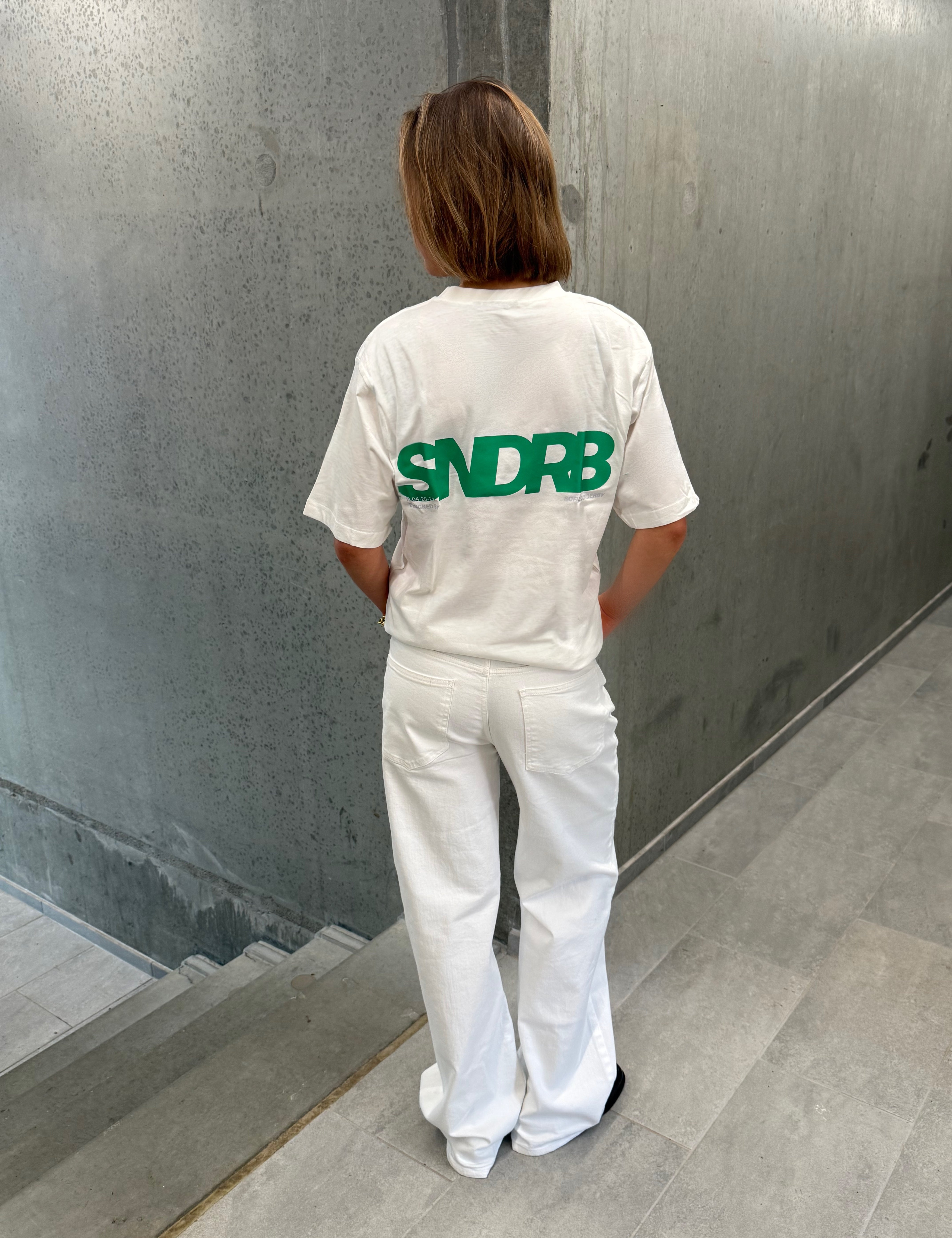 Stemningsbillede af pige der bærer en hvid t-shirt med grønt SNDRB tryk og blå NANNA jeans.  Fra BySofieSønderby