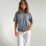 Modelfoto af pige som bærer en SNDRB tee i farven stone, samt et par hvide jeans. Alt fra By Sofie Sønderby