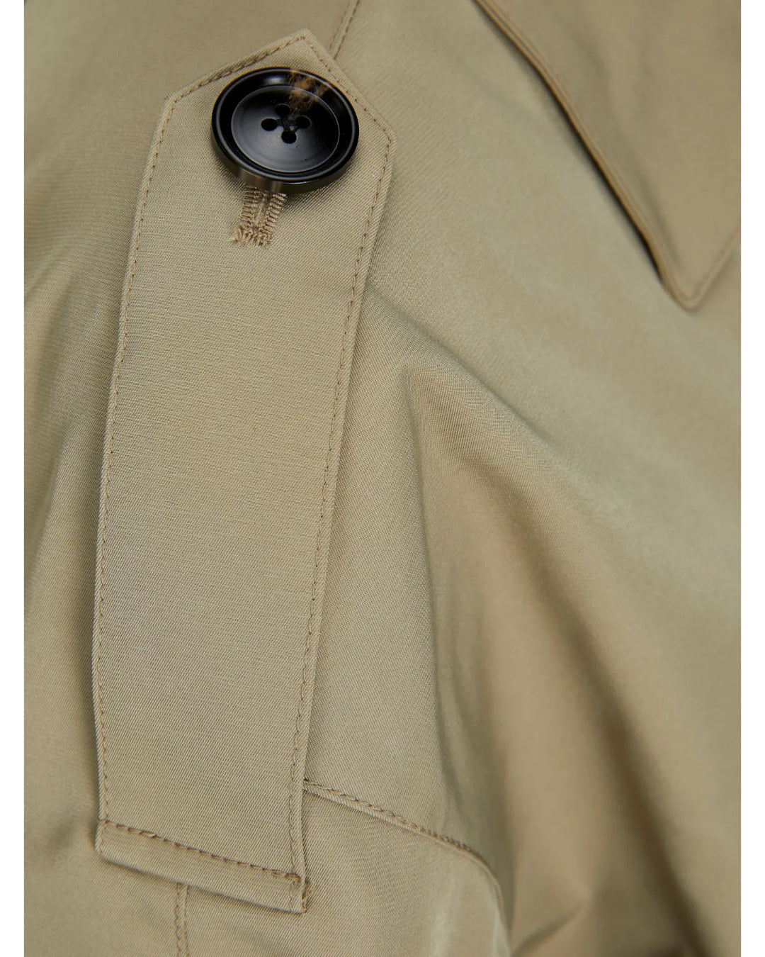 En beige jakke har en detalje med en mørk knap fastgjort til et skulderstrop. Stoffet er jævnt og syet sammen med synlige sømme.