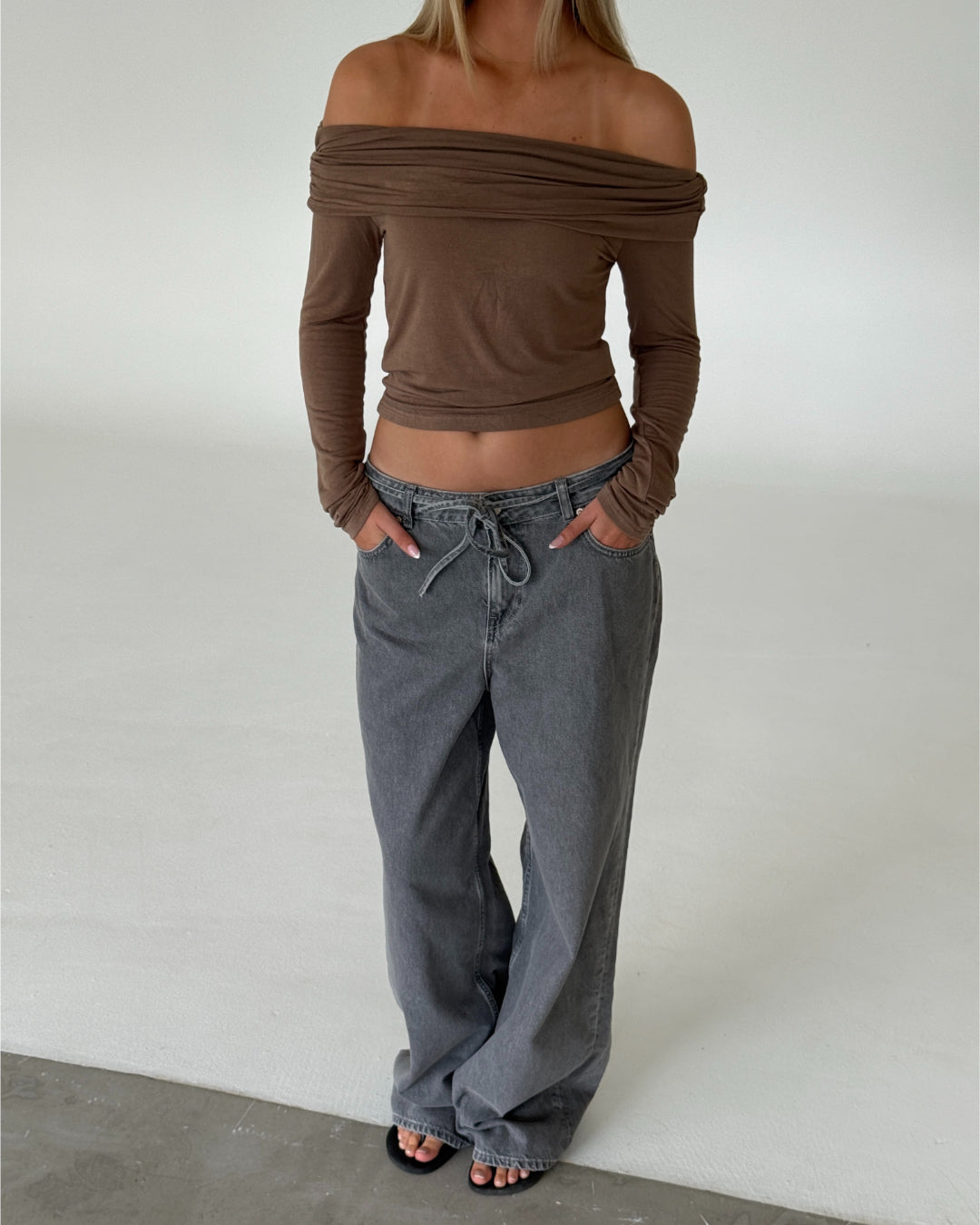 Modelbillede af TARA off shoulder bluse, brun og EDA wide leg jeans, grå. Begge fra BySofieSønderby