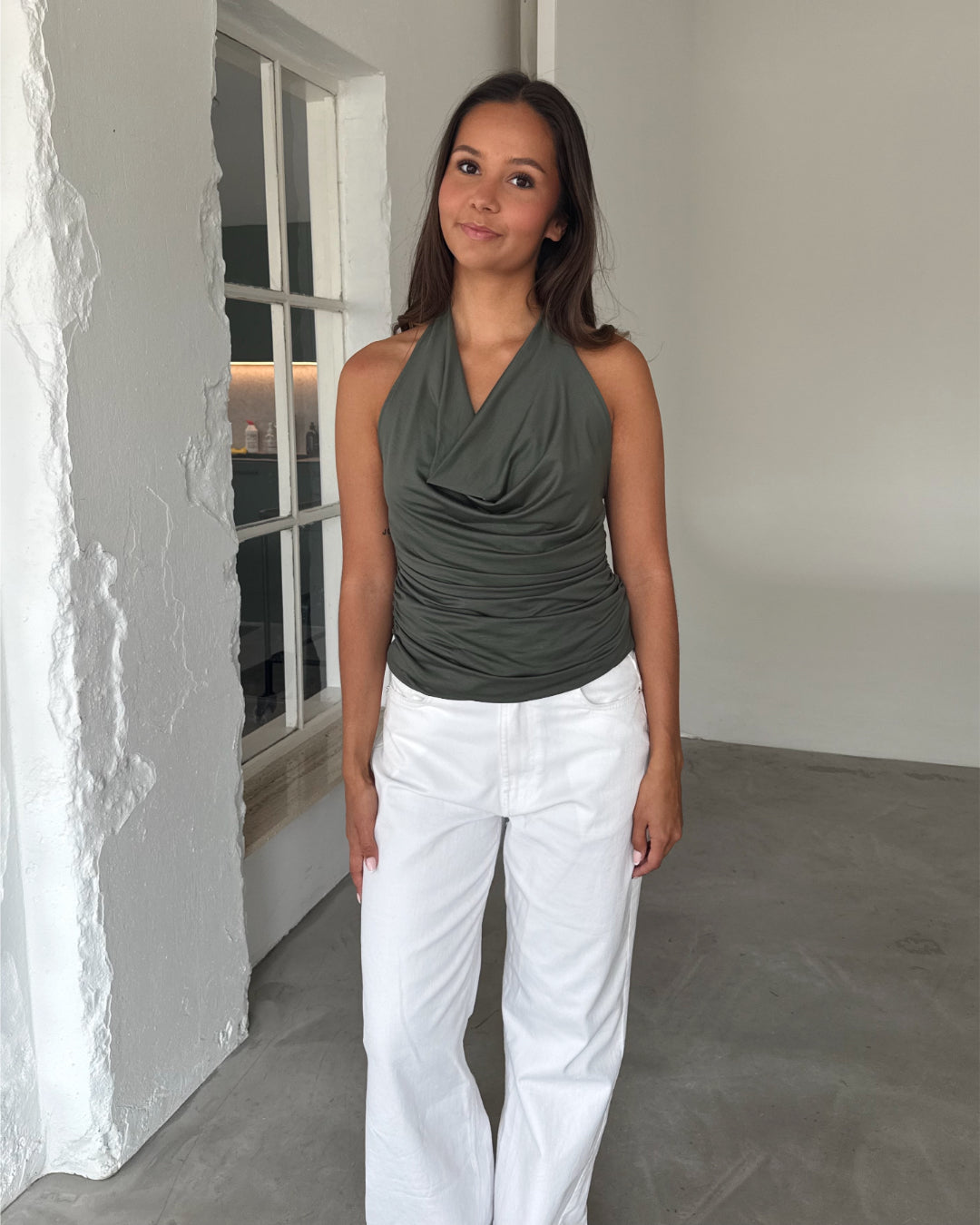 Modelfoto af pige som bærer en kakifarvet TAYLOR halterneck top, samt en hvide jeans. Alt er fra BySofieSønderby