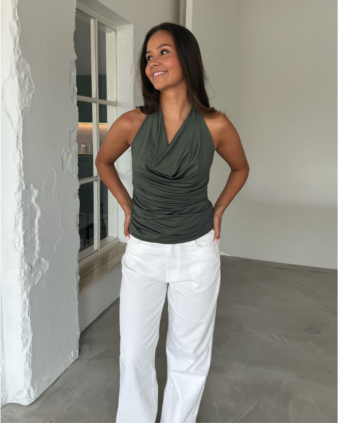 Modelfoto af pige som bærer en kakifarvet TAYLOR halterneck top, samt en hvide jeans. Alt er fra BySofieSønderby