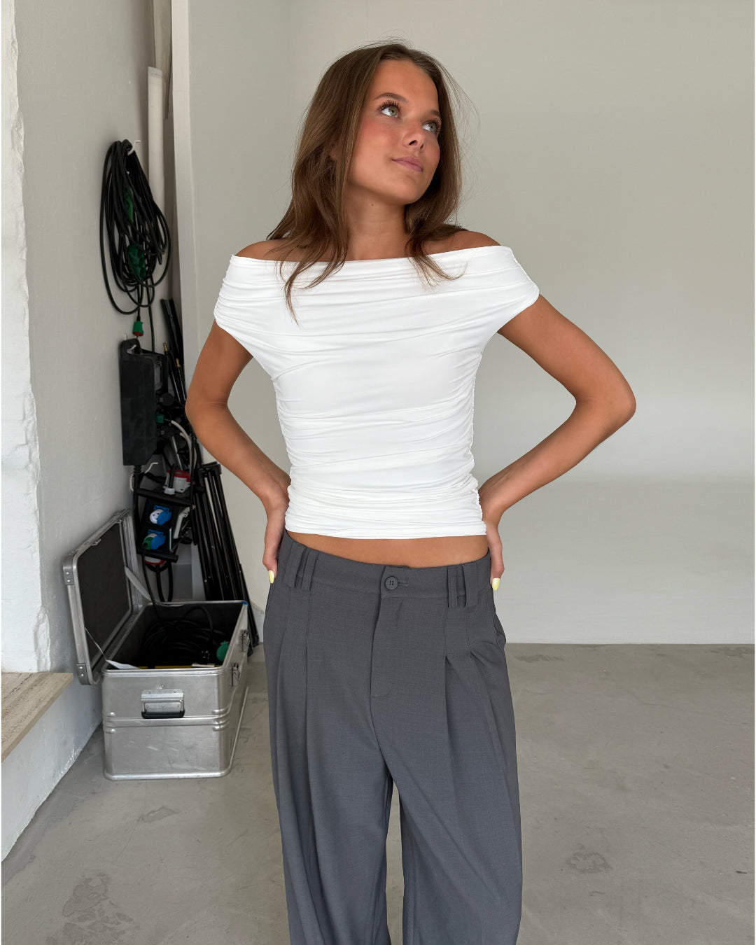 Modelfoto af pige som bærer hvid THORA offshoulder top og grå habitbukser . Alt er fra BySofieSønderby