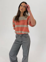 En person iført en stribet sweater og grå jeans står afslappet, mens de kigger opad i et lyst miljø.
