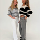 To kvinder står sammen, iført stribede trøjer; den ene i grå med hvide bukser og den anden i sort med grå bukser, i et lyst rum.