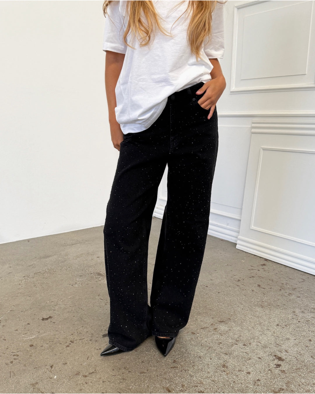 Modelfoto af pige i sorte TOKYO jeans med sorte sten foran, samt hvid basic t-shirt. Alt er fra BySofieSønderby